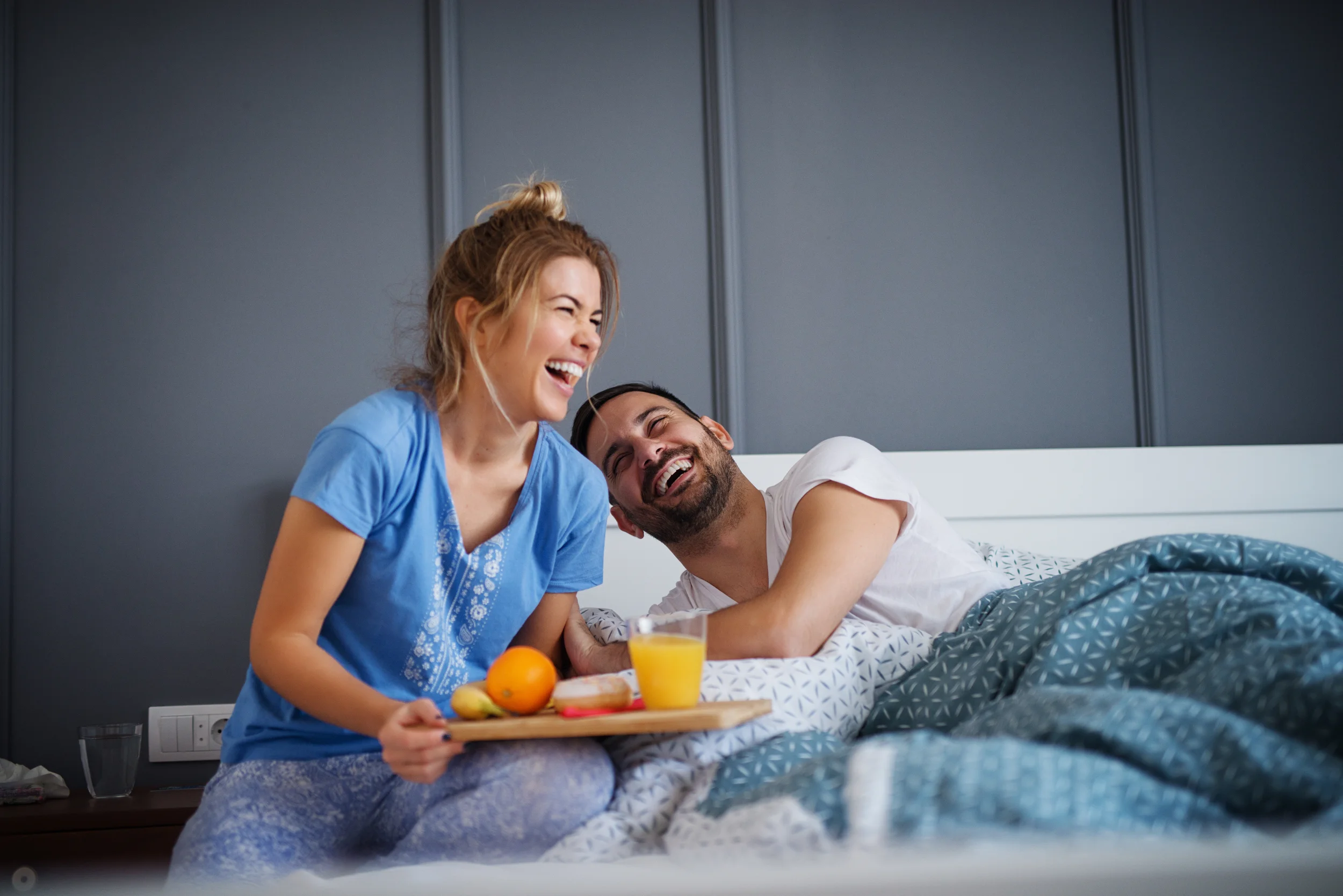 couple siting in bed laughing while breakfast is served